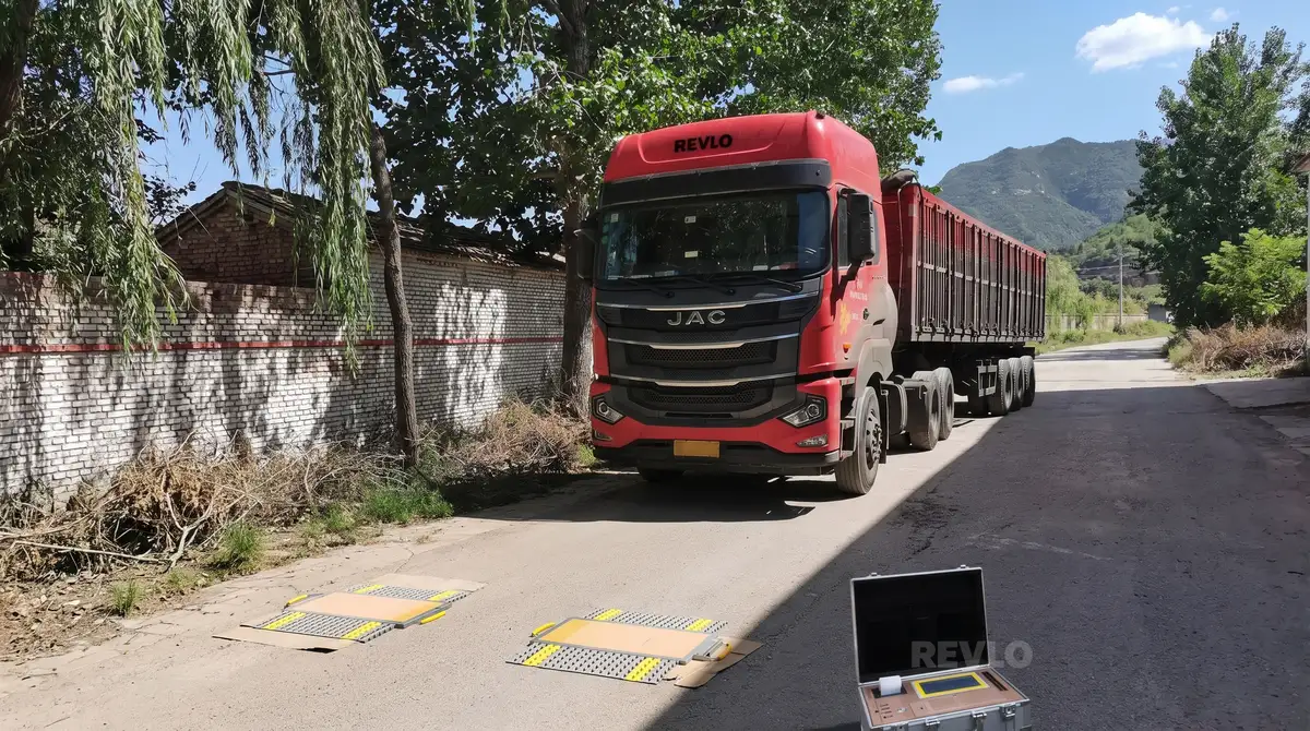 Caminhão com carreta basculante parado sobre as plataformas da balança móvel, com a maleta do display aberta no chão ao lado