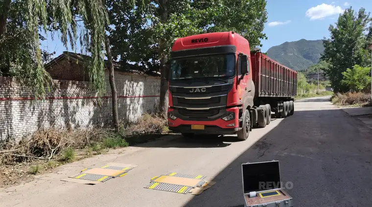 Caminhão com carreta basculante parado sobre as plataformas da balança, com a maleta do display aberta no chão ao lado